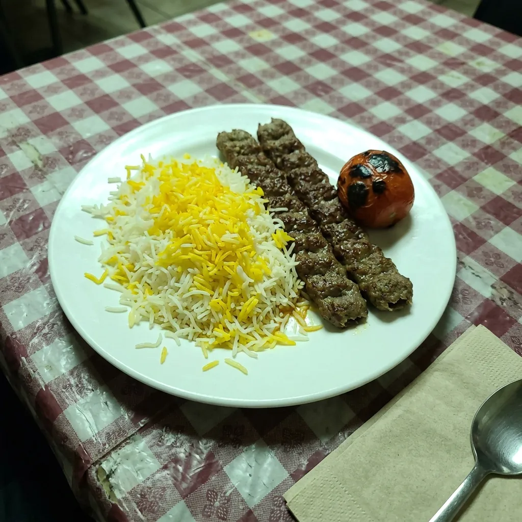 عکس موبایلی بشقاب چلوکباب روی رومیزی چهارخانهٔ پلاستیکی